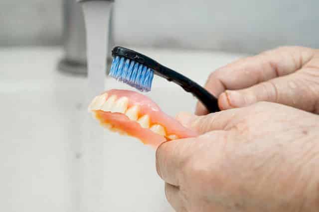 patient use toothbrush to clean partial denture of replacement teeth.